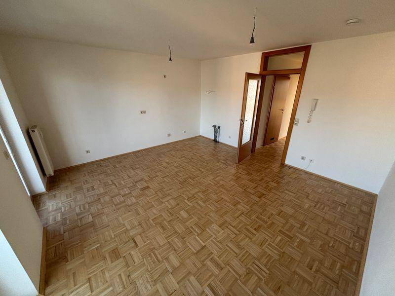 Geräumiges Wohnzimmer mit hellem Parkettboden und Holztür, bereit zur individuellen Gestaltung.