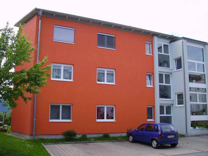 Seitenansicht eines Wohnhauses mit leuchtend oranger Fassade, großen Fenstern und einem geparkten Auto.
