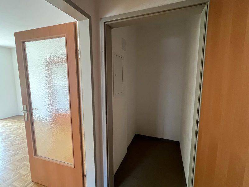 Flur mit Zugang zu einem Zimmer mit Parkettboden und einer praktischen Abstellnische.