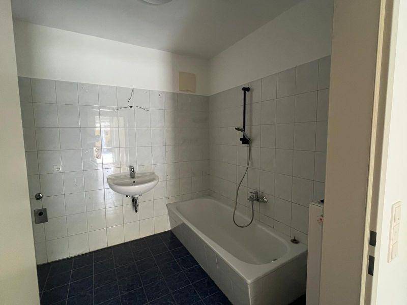 Badezimmer mit weißen Wandfliesen, dunkelblauem Boden und einer Badewanne sowie einem Waschbecken.