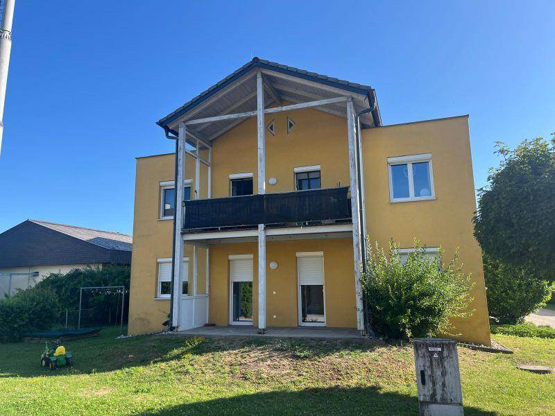 Gelbes Mehrfamilienhaus mit Balkonen und überdachtem Erdgeschossbereich, umgeben von Grünflächen.