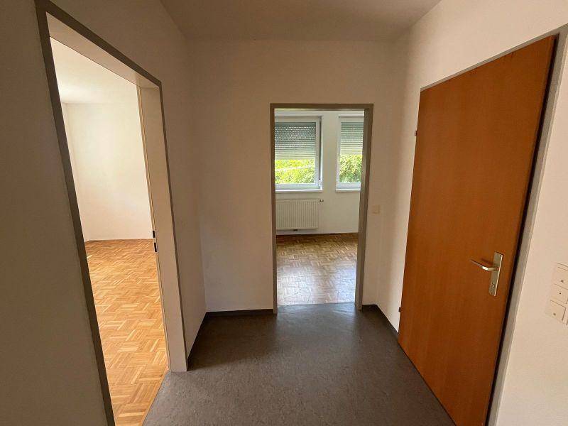 Heller Flur mit Türen zu verschiedenen Zimmern, eines davon mit Parkettboden und Fensterrollläden.
