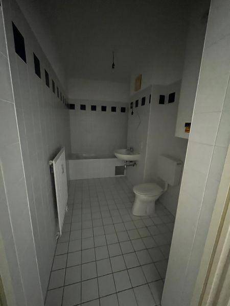 Badezimmer mit weißen Fliesen, Badewanne, WC und Waschbecken, akzentuiert durch schwarze Bordüren.