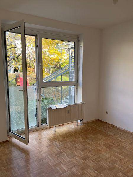 Heller Raum mit Parkettboden und großer Fensterfront, die viel Tageslicht hereinlässt.