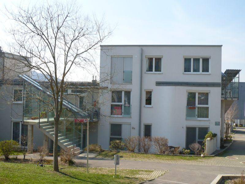 Ansicht des modernen Wohngebäudes mit großen Fenstern und umliegender Grünfläche an einem sonnigen Tag.