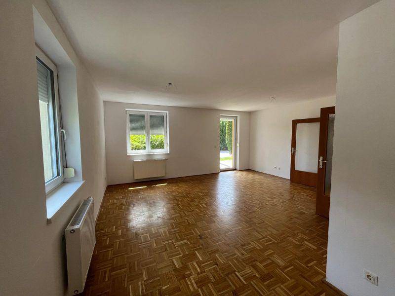 Geräumiges Wohnzimmer mit Parkettboden, hellen Wänden und mehreren Fenstern für viel Tageslicht.