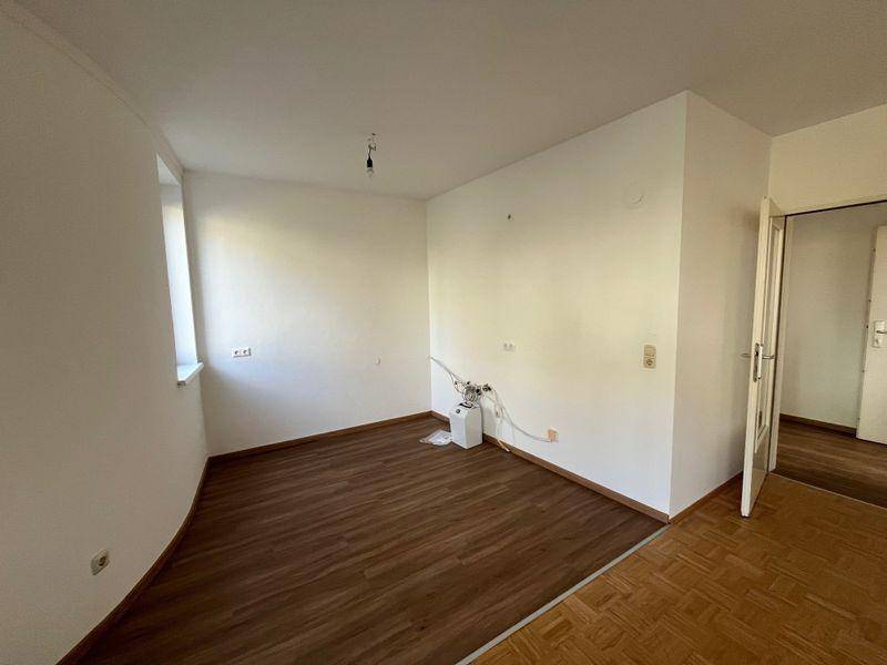 Heller, leerer Raum mit Laminatboden und weißen Wänden, bereit zur individuellen Gestaltung.