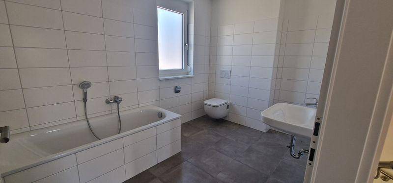 Helles Badezimmer mit weißen Fliesen, Badewanne und modernem Waschbecken.