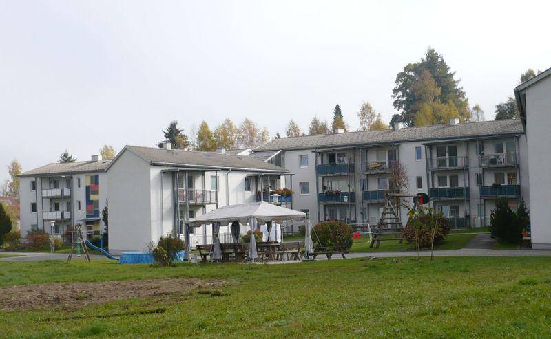 Wohnanlage mit mehreren Gebäuden, Balkonen, einem Spielplatz und einer gemeinschaftlichen Sitzgelegenheit im Freien.