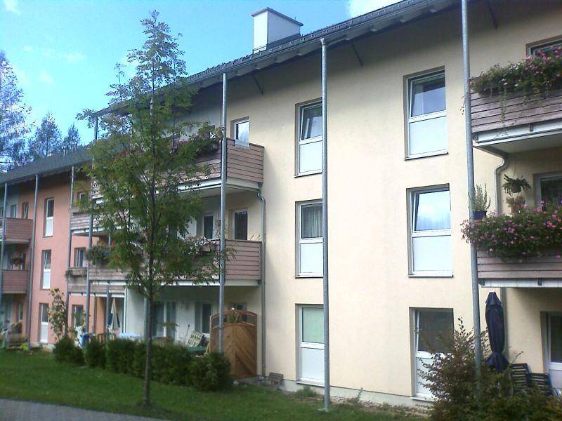 Fassade eines Mehrfamilienhauses mit Balkonen und Blumenkästen unter klarem Himmel.