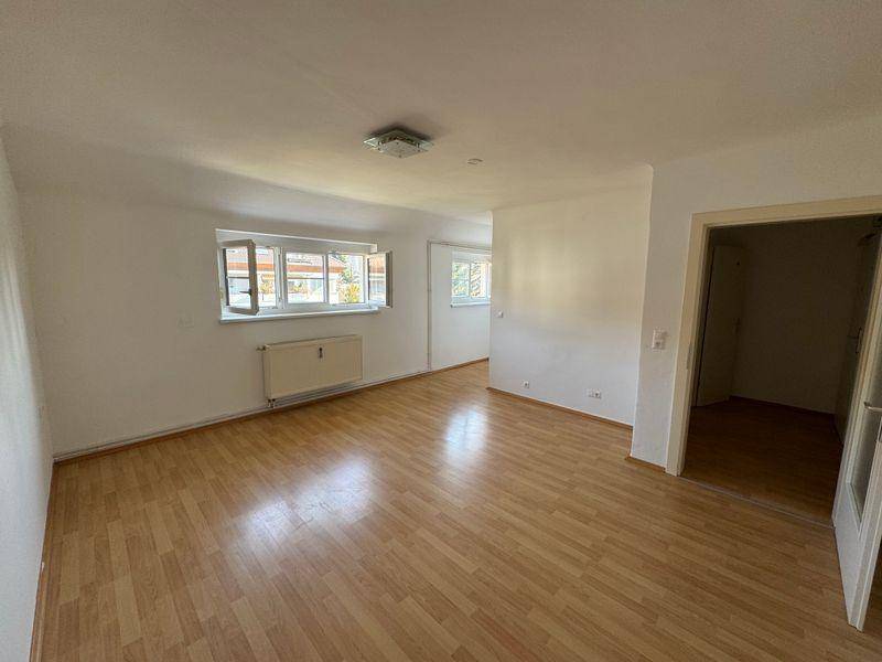 Freundlicher, leerer Raum mit Laminatboden und Fenstern, die viel Tageslicht hereinlassen, mit Türzugang.