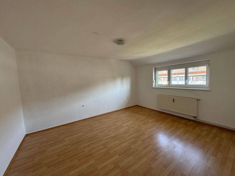 Heller, leerer Raum mit Laminatboden, weißen Wänden und einem Fenster mit Blick nach draußen.