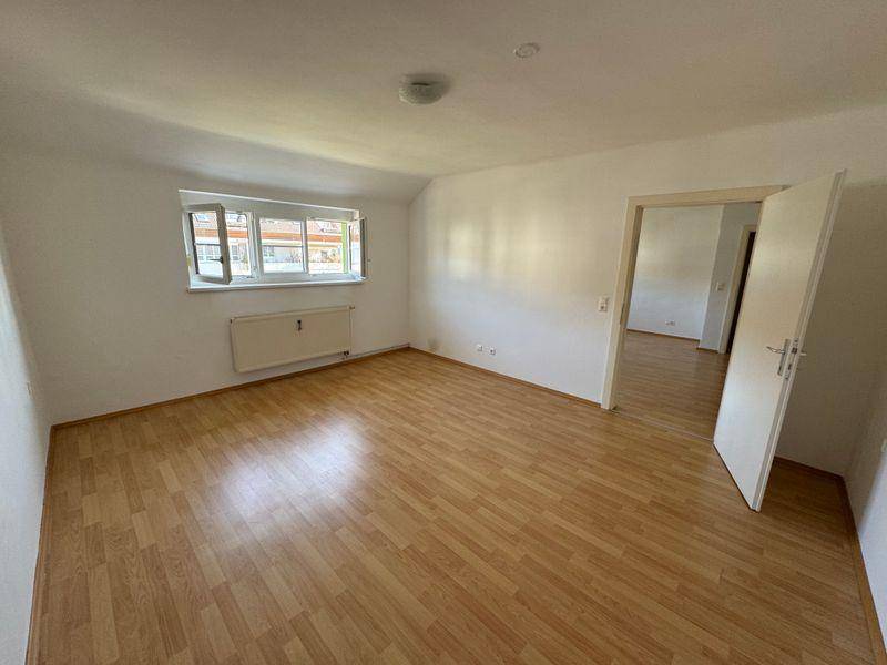 Geräumiger, heller Raum mit Laminatboden und Zugang zu einem weiteren Zimmer, ideal als Wohnbereich.