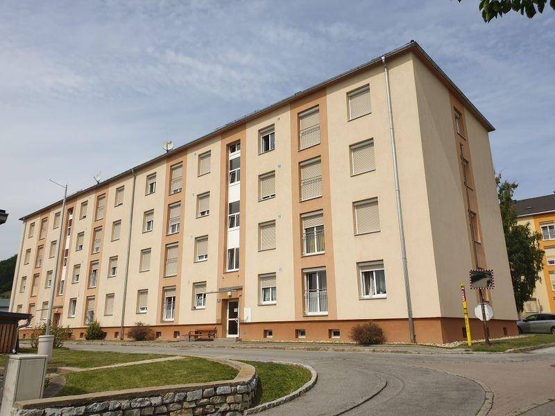 Gepflegtes Mehrfamilienhaus mit beiger Fassade und Rollläden an den Fenstern unter bewölktem Himmel.