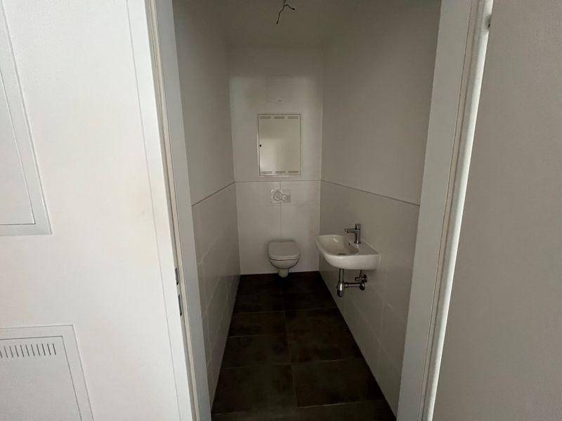 Kleines Gäste-WC mit Toilette, Waschbecken und Wandspiegel in schlichtem Design.