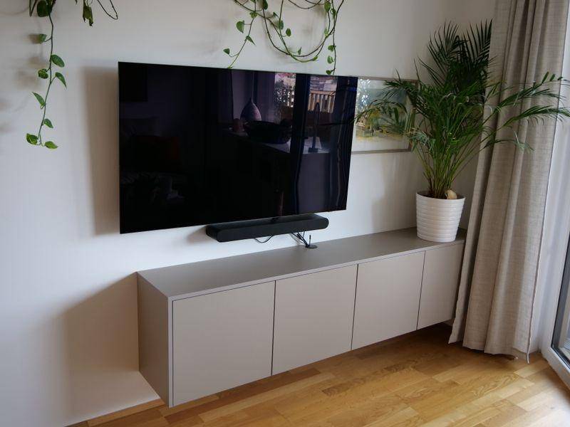Modernes Wohnzimmer mit wandmontiertem Fernseher, schwebendem Unterschrank und Grünpflanzen.