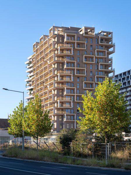 Modernes Hochhaus mit gestaffelten Balkonen und zeitgenössischer Fassadengestaltung von der Straße aus gesehen.