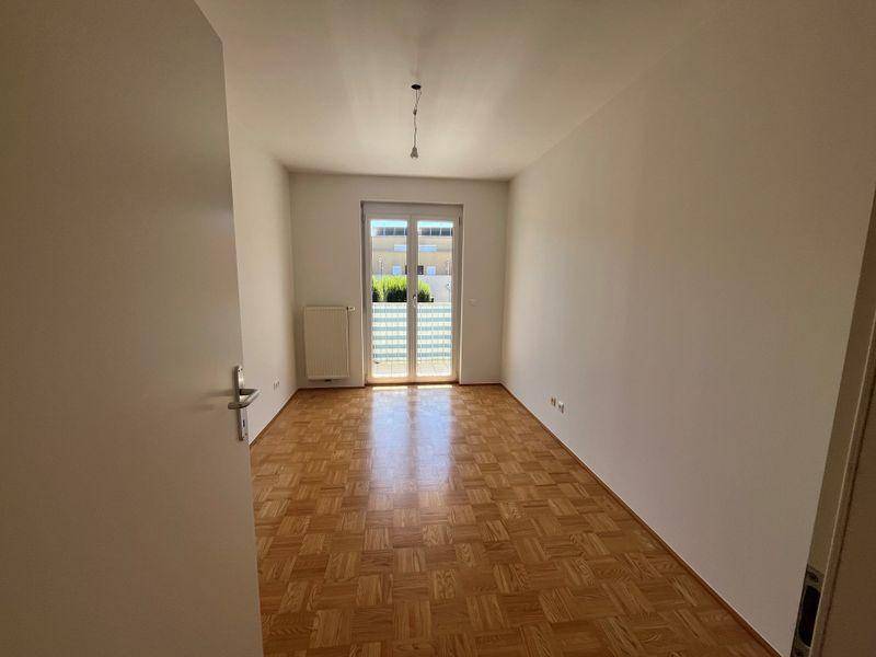 Weiteres Schlafzimmer mit Parkettboden, weißen Wänden und Zugang zu einem Balkon mit Sichtschutz.
