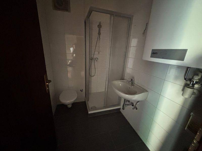 Kleines Badezimmer mit Duschkabine, WC, Waschbecken und Warmwasserboiler.