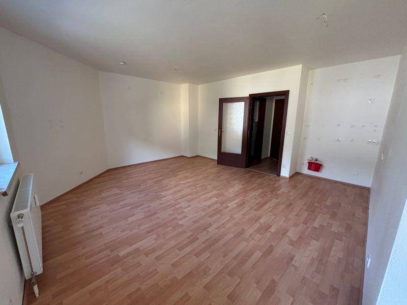 Geräumiges, unmöbliertes Zimmer mit Laminatboden und Zugang zu weiteren Räumen.