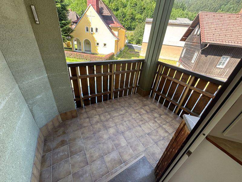 Gefliester Balkon mit Holzgeländer und Blick auf die Nachbarschaft und grüne Hügel.