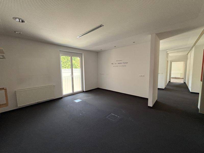 Großer offener Bürobereich mit dunklem Teppichboden, weißen Wänden und viel Tageslicht.