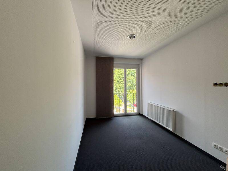 Leerer Raum mit dunklem Teppichboden, weiß gestrichenen Wänden und Balkonzugang.