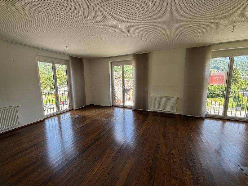 Geräumiger Wohnbereich mit dunklem Holzfußboden und mehreren Balkonzugängen, bietet viel natürliches Licht.