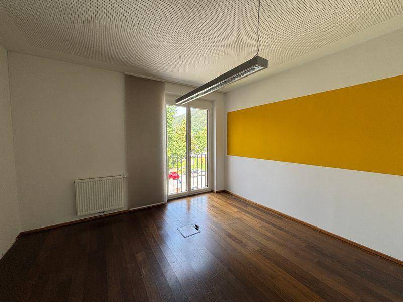 Heller Raum mit dunklem Holzfußboden, gelber Akzentwand und Zugang zu einem Balkon.