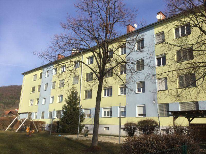 Mehrfamilienhaus mit farbiger Fassade und Spielplatz im Vordergrund unter blauem Himmel.