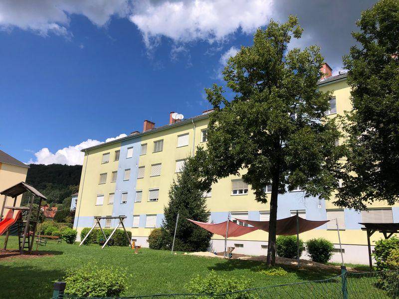 Mehrfamilienhaus mit Spielplatz und Bäumen unter blauem Himmel, einladende Außenanlage.