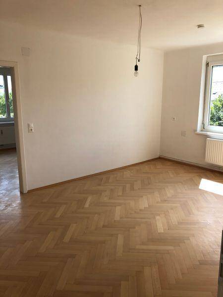 Geräumiges Zimmer mit Fischgrätparkett und viel Tageslicht, unmöbliert und hell.