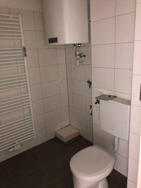 Badezimmer mit Toilette, Heizkörper und Boiler, weiß gefliest und praktisch gestaltet.