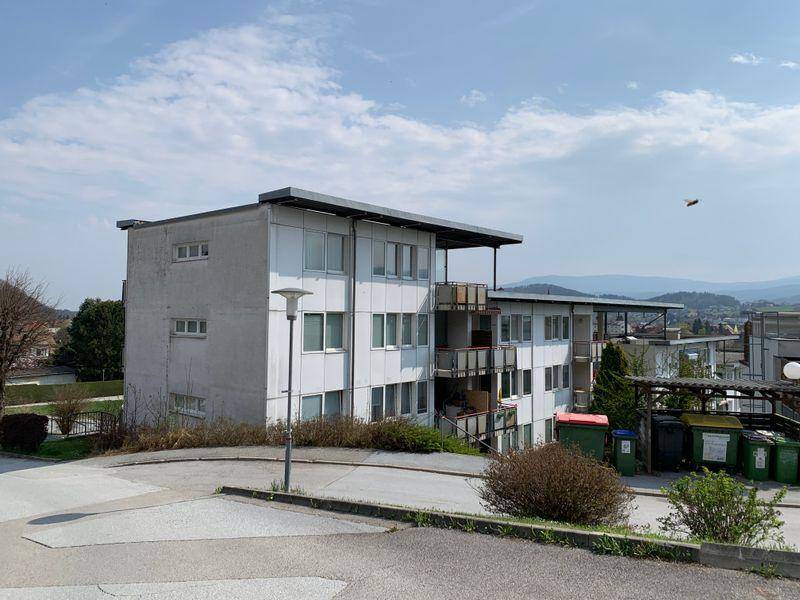 Mehrfamilienhaus mit mehreren Balkonen und Blick auf die umliegende Landschaft und Berge.