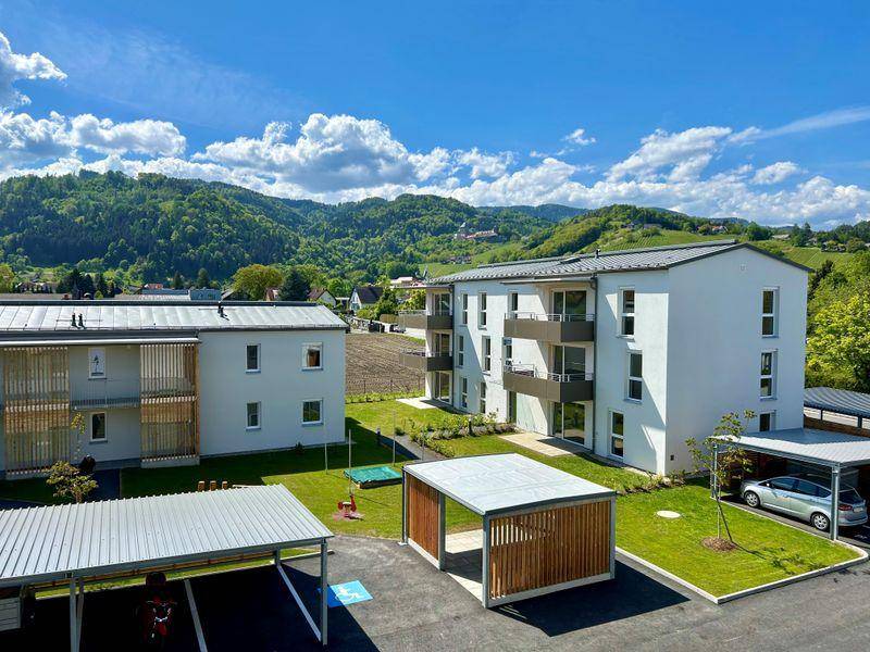 Neubau-Wohngebäude mit Balkonen und überdachten Stellplätzen, eingebettet in eine idyllische grüne Umgebung.