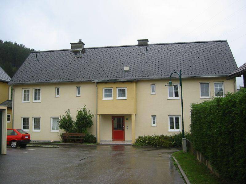 Gepflegtes Mehrfamilienhaus mit heller Fassade, Satteldach und Parkplätzen im Freien an einem regnerischen Tag.