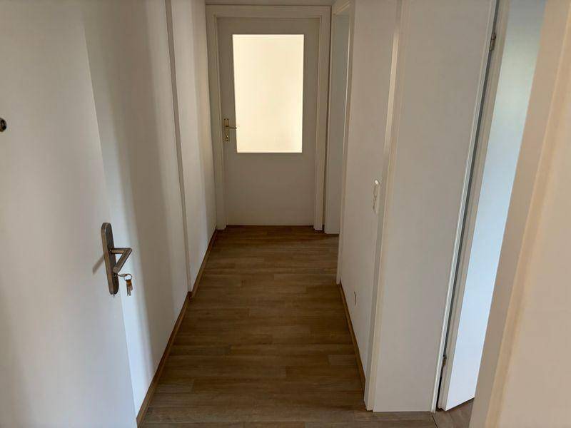 Heller Flur mit Laminatboden und weißen Wänden, der zu weiteren Räumen führt.