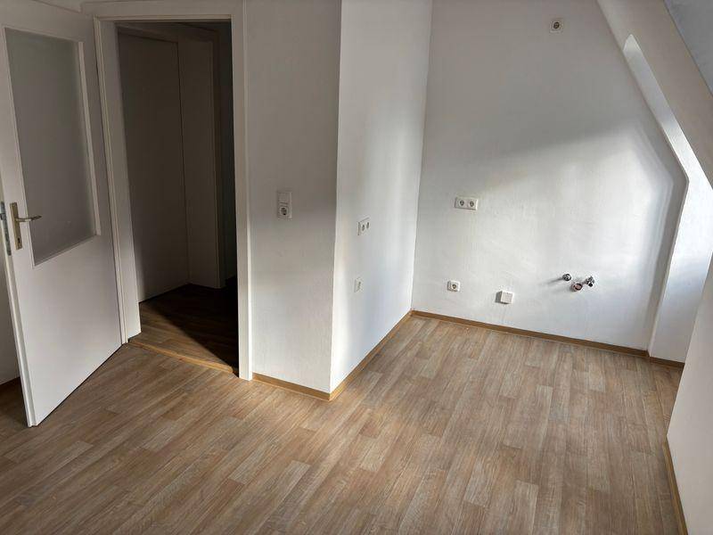 Leerer Raum mit Dachschräge, Laminatboden und sichtbaren Anschlüssen an der Wand.