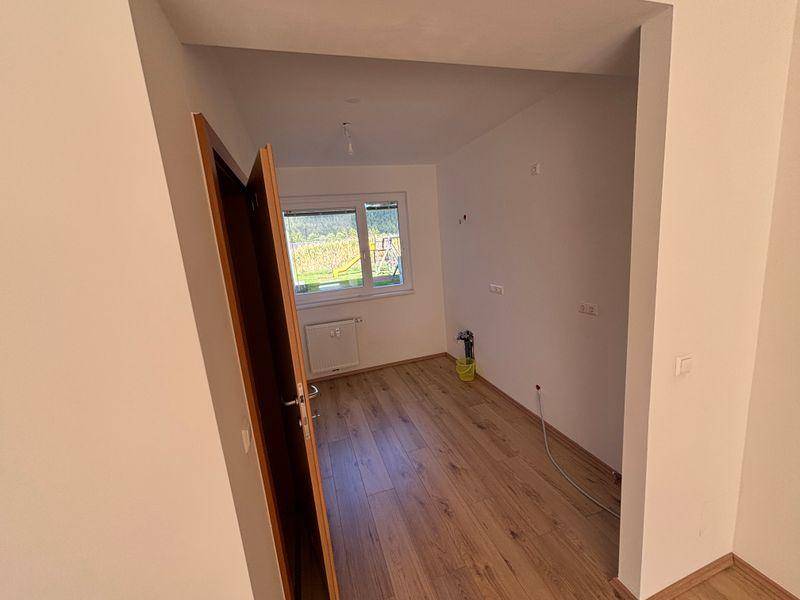 Helles Zimmer mit Laminatboden und Fenster, das einen Blick ins Grüne bietet.