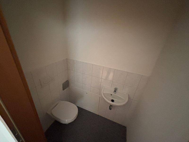 Separates Gäste-WC mit Toilette, kleinem Waschbecken und weißen Fliesen im unteren Bereich.