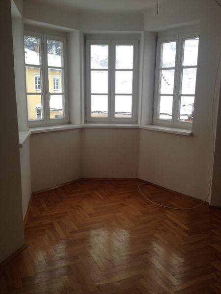 Heller Raum mit Fischgrätparkett und einem Erkerfenster mit Blick nach draußen.