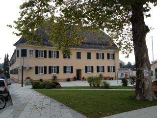 Historisches Gebäude mit gepflegter Fassade, Rasenfläche und altem Baum im Vordergrund.
