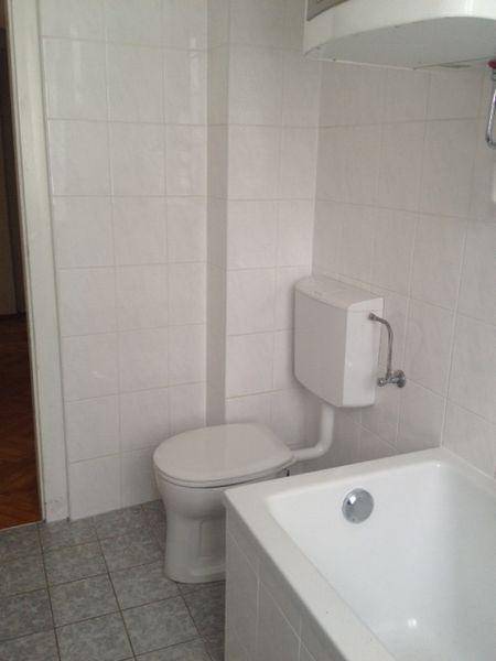Badezimmer mit weiß gefliesten Wänden, Toilette und Badewanne.