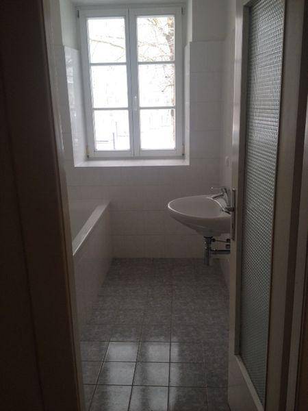 Helles Badezimmer mit Badewanne, Waschbecken und Fenster, durch eine Türöffnung gesehen.