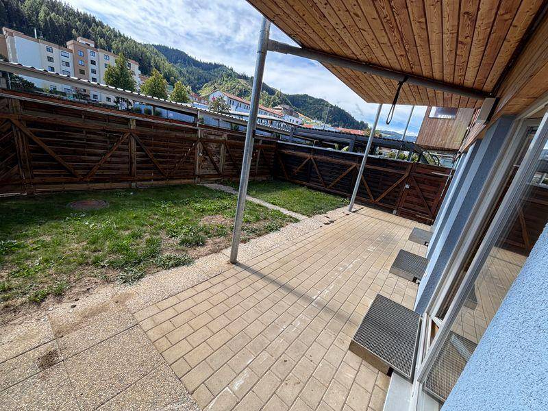 Gepflasterte Terrasse mit kleinem Gartenbereich und Blick auf die umliegenden grünen Hügel.