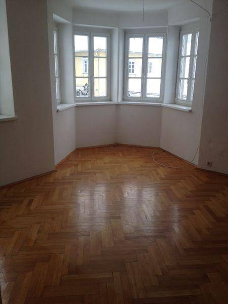 Geräumiger Raum mit Fischgrätparkettboden und einem hellen Erkerfensterbereich.
