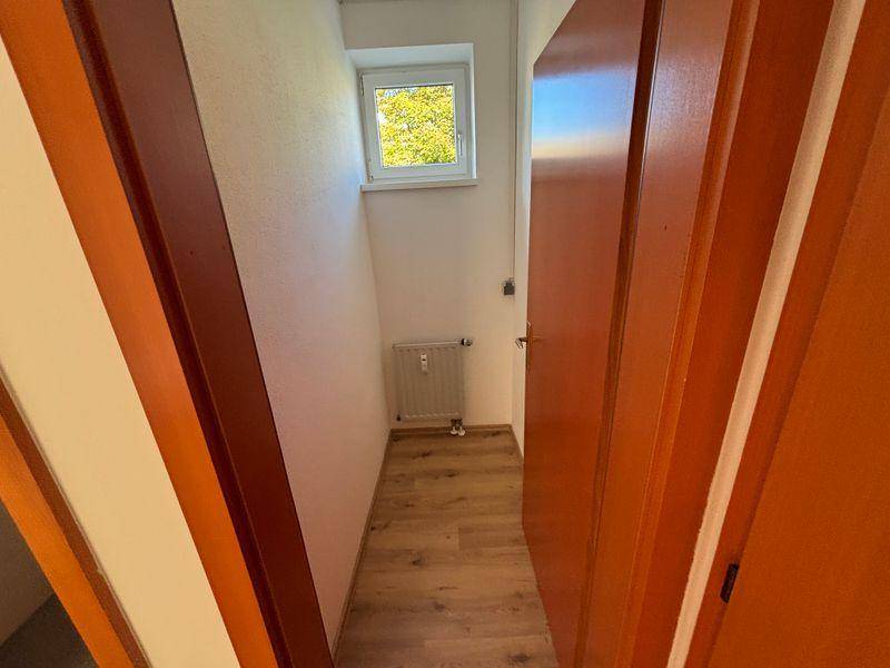 Schmaler Flurbereich mit Fenster, Heizkörper und Laminatboden.