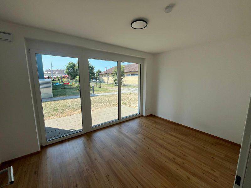 Geräumiger Raum mit Holzboden und großen Glasschiebetüren zum Außenbereich.