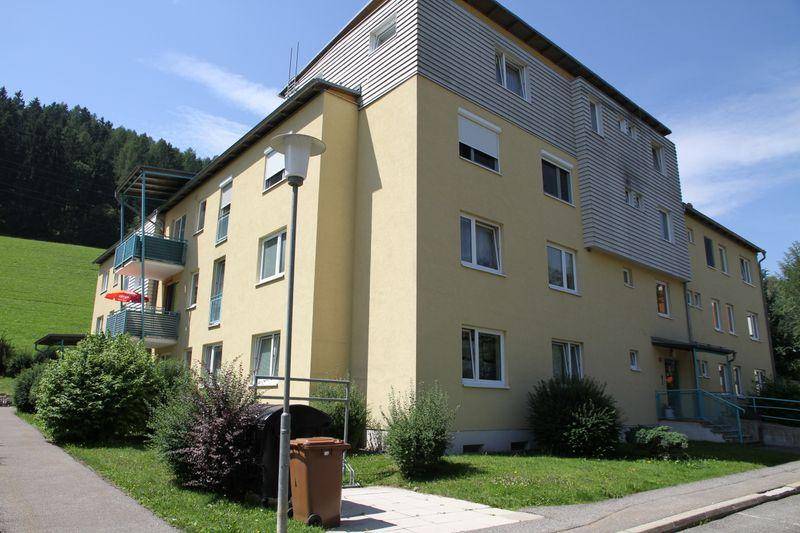 Mehrfamilienhaus mit Balkonen und grüner Umgebung am Hang gelegen.