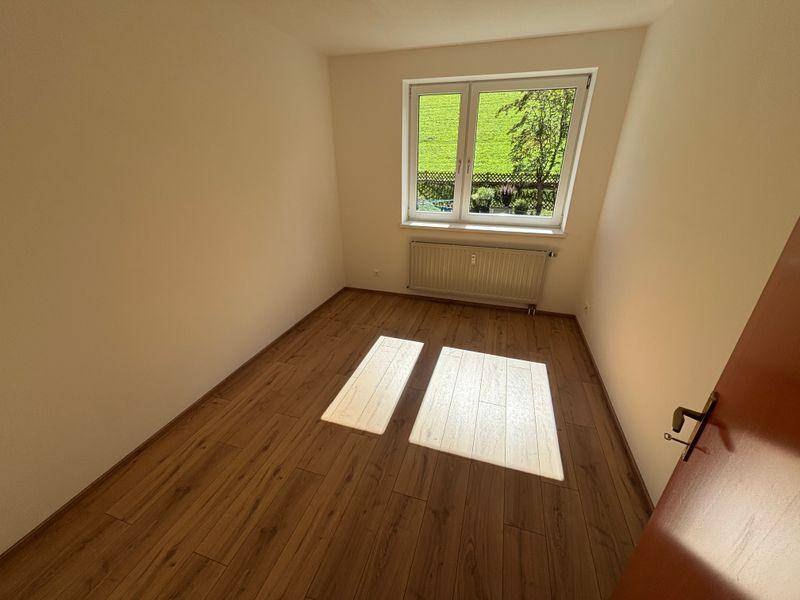 Helles Schlafzimmer mit Laminatboden und Blick ins Grüne durch das Fenster.